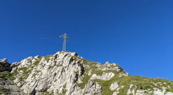 Giewont, śpiący rycerz, wznosi się ku błękitnemu niebu. Na szczycie stoi krzyż, a pod nim skaliste zbocza porośnięte trawą.