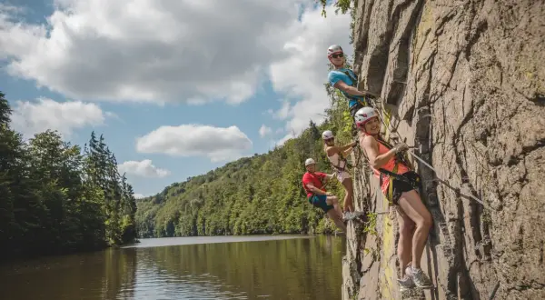Grupa przyjaciół pokonuje via ferrata w Czechach, wspinając się po skalnej ścianie nad malowniczą rzeką.