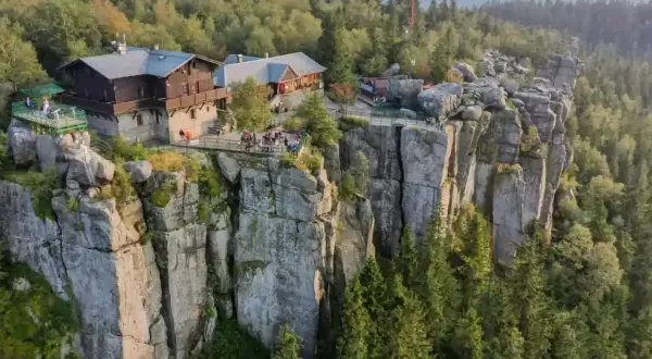 Góry Stołowe z górującymi nad lasem skalnymi formacjami i schroniskiem na szczycie.