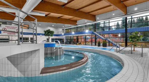 Wodny świat w aquaparku Špindlerův Mlýn: basen z wodospadem, jacuzzi i widokiem na las.