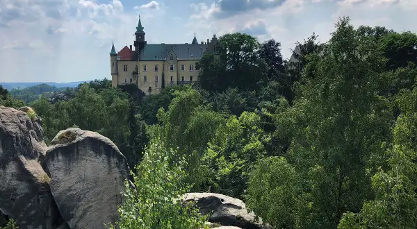 Zamek Hrubá Skála wznosi się dumnie nad skalistym krajobrazem, otoczony bujną zielenią drzew.