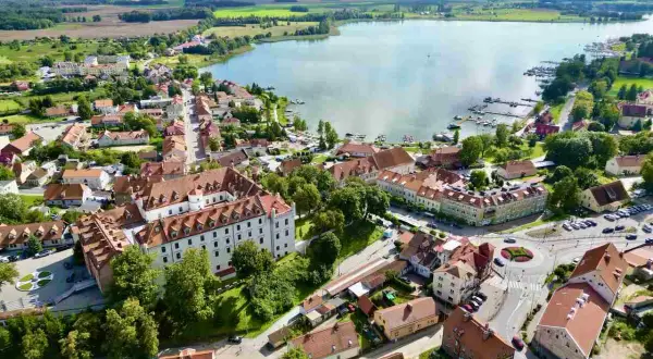 Malownicze miasteczko nad jeziorem, gdzie białe budynki z czerwonymi dachami tworzą urokliwy krajobraz. To prawdziwa kraina tysiąca jezior, pełna zieleni i spokoju.