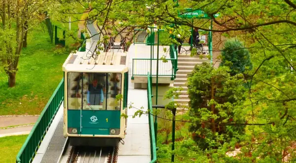 Kolejka linowa Praga w zieleni. Wagonik z numerem 1 zbliża się do stacji, otoczony bujną roślinnością.