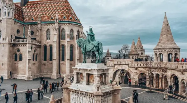 Budapeszt stare miasto: Rycerz na koniu przed kościołem z kolorowym dachem i basztami. Turyści spacerują po brukowanym placu.