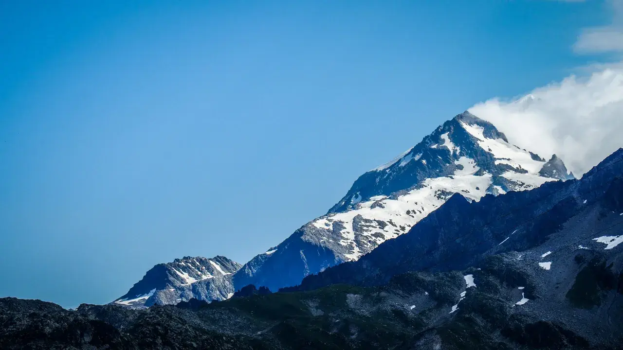 Majestatyczne szczyty Alp, pokryte śniegiem, z chmurami otulającymi wierzchołek. Widok na wejście na Mont Blanc.
