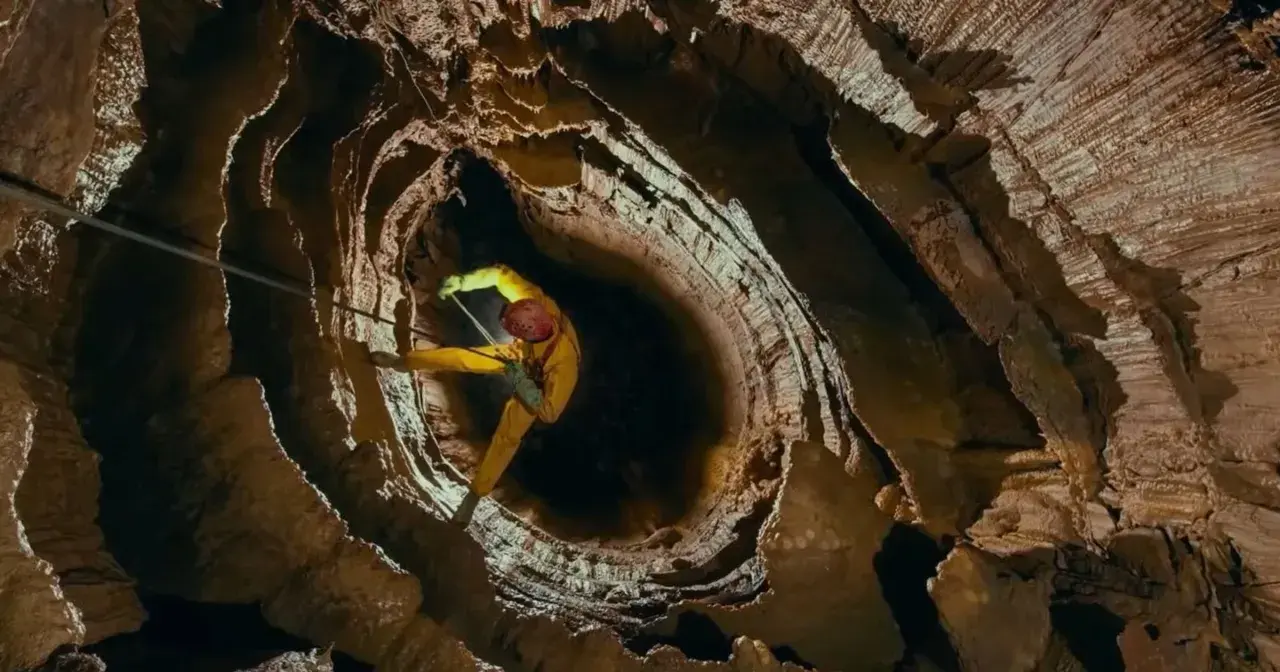 Speleolog w żółtym kombinezonie zjazduje w głąb skalnej otchłani, eksplorując potencjalnie najgłębszą jaskinię na świecie.