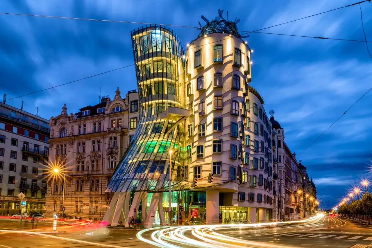 Tańczący dom w Pradze, nocą, z rozmazanymi światłami samochodów na ulicy.