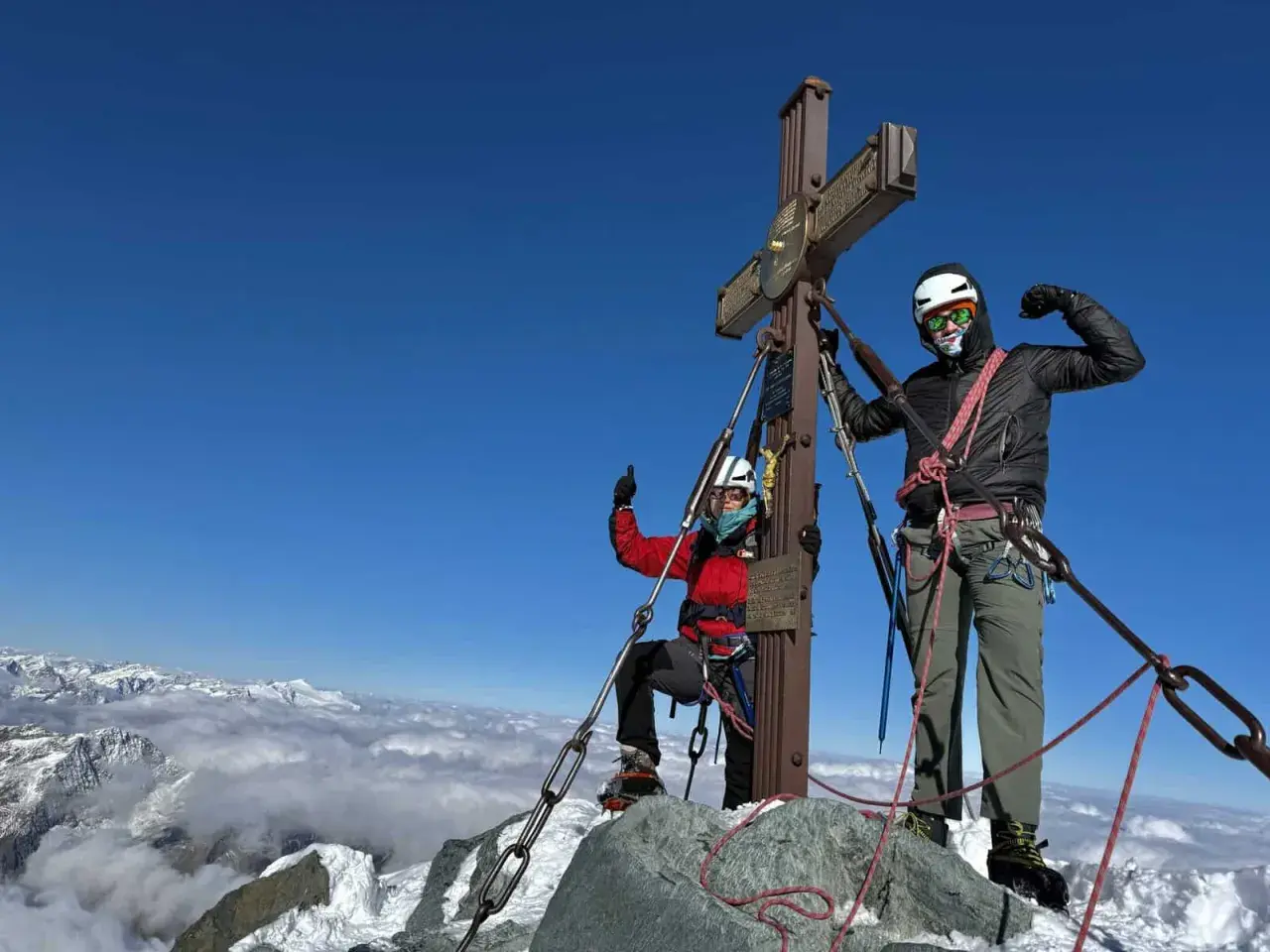 Dwóch alpinistów na szczycie Grossglockner, najwyższy szczyt Austrii. W tle morze chmur i ośnieżone góry.