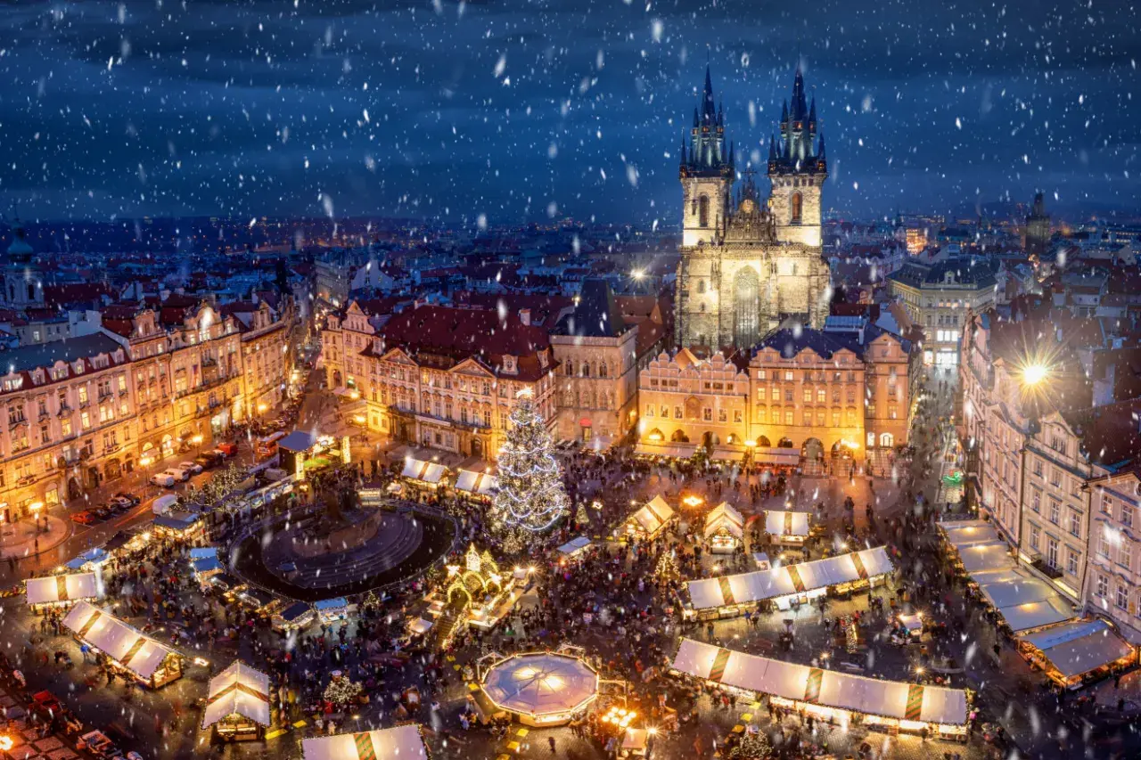 Tłoczny jarmark bożonarodzeniowy w Pradze, z oświetloną choinką i kościołem w tle, to jeden z najpiękniejszych jarmarków bożonarodzeniowych w Europie.