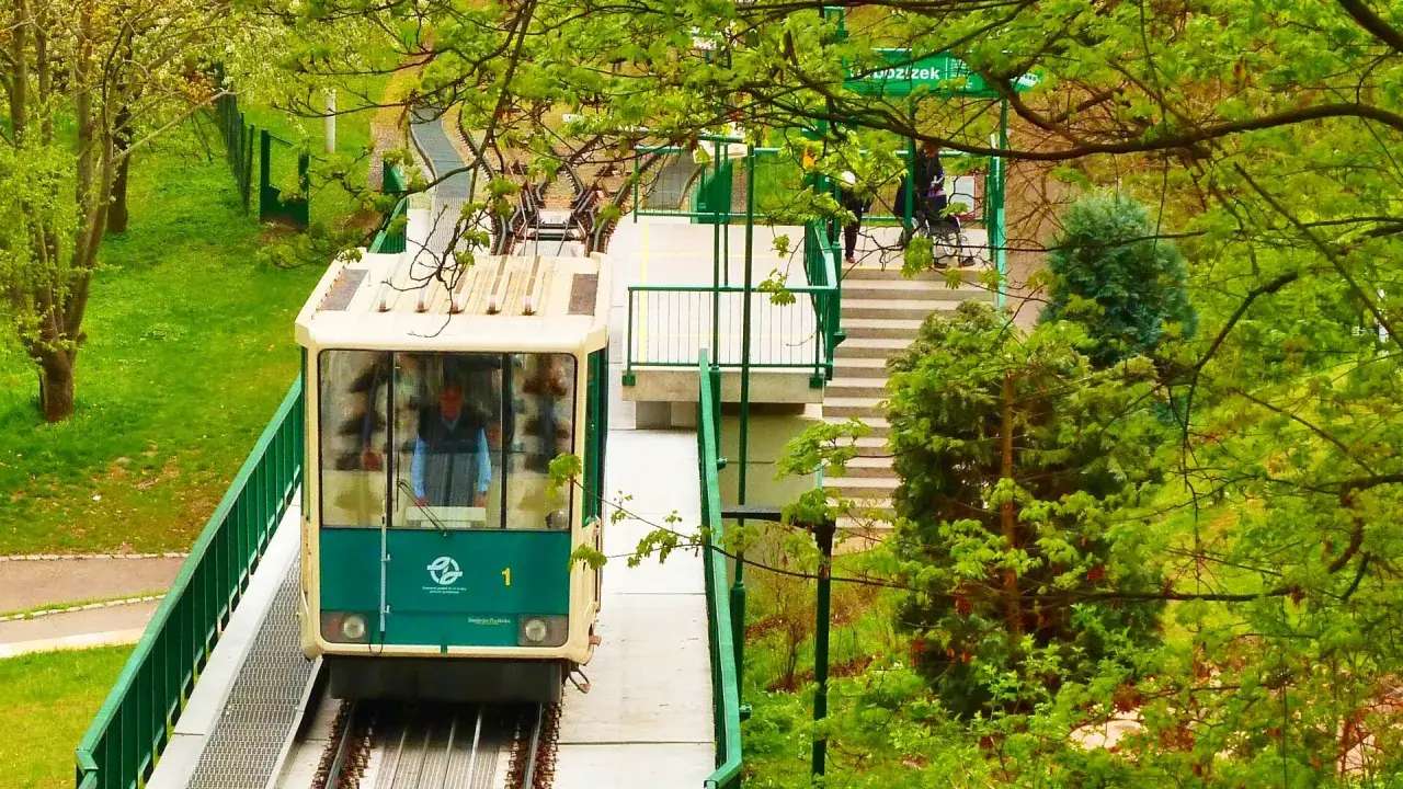 Kolejka linowa Praga w zieleni. Wagonik z numerem 1 zbliża się do stacji, otoczony bujną roślinnością.