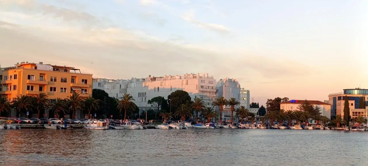 Zadar: nadmorska promenada z palmami, łodziami i nowoczesnymi budynkami w ciepłym świetle zachodzącego słońca. Idealne miejsce, by zobaczyć piękno Adriatyku.