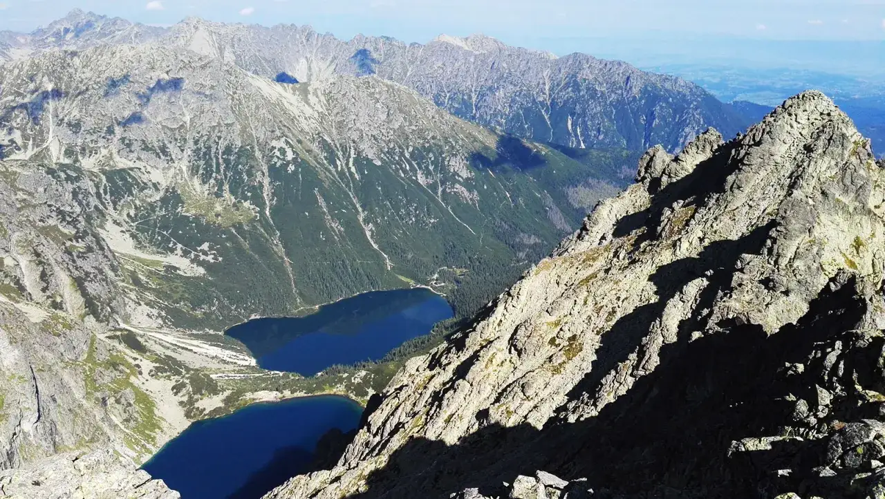 Widok z Rys&oacute;w na Morskie Oko i otaczające szczyty. Dwa jeziora lśnią w dolinie, otoczone stromymi, skalistymi zboczami.