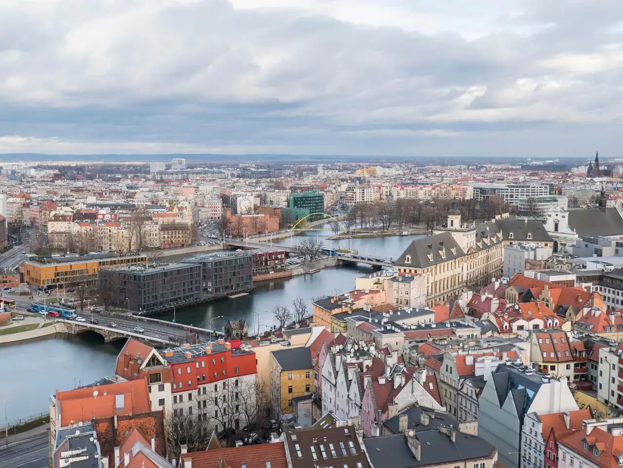 Widok na Wrocław z wieży widokowej. Rzeka Odra przecina miasto, a w oddali widać zabudowania i zielony most. To idealne miejsce, by podziwiać wieże widokowe Dolny Śląsk.