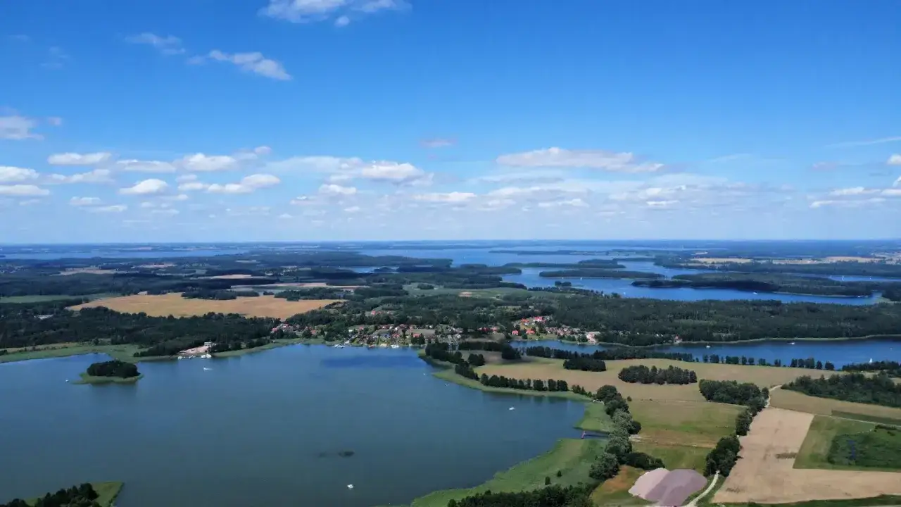 Malownicza kraina tysiąca jezior, z licznymi wyspami, lasami i polami, pod błękitnym niebem z białymi chmurami.