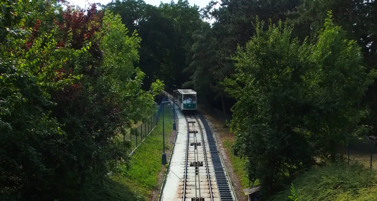 Zielona kolejka linowa Praga wspina się po stromym zboczu wśr&oacute;d bujnej zieleni.