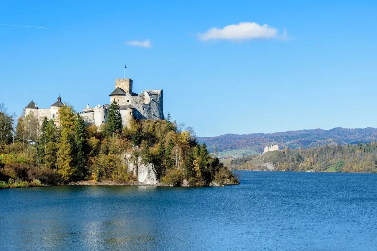 Zamek na skale nad jeziorem, jesienne drzewa, góry w tle. Idealne miejsce, gdzie w góry.