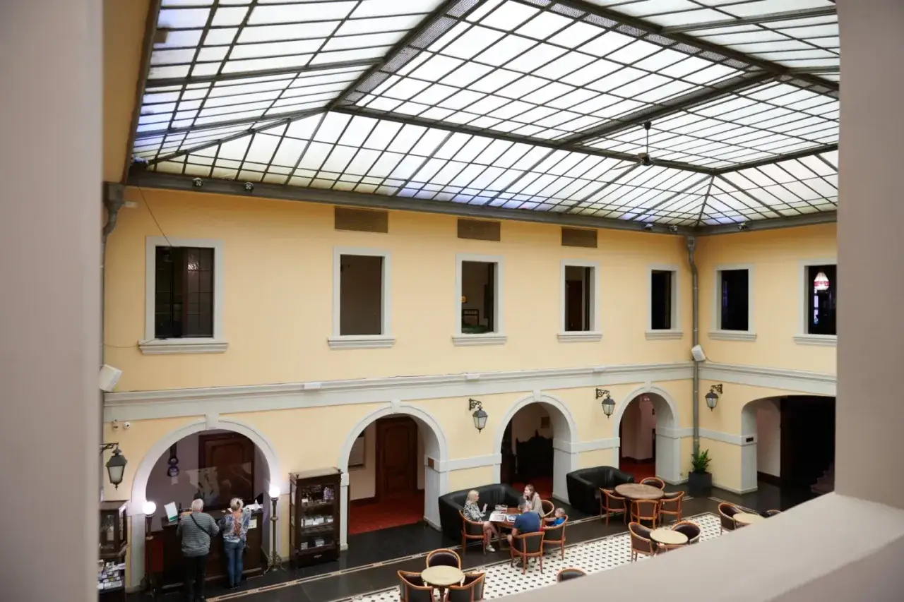 Wnętrze hotelu w Polsce z przeszklonym dachem. Ludzie siedzą przy stolikach, a przy recepcji stoi para.
