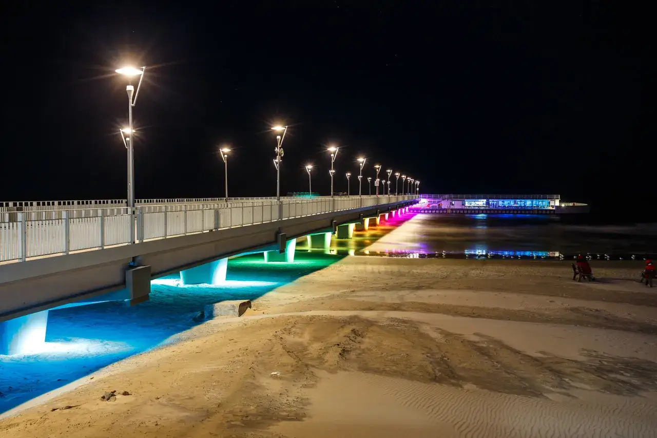 Kolobrzeg atrakcje zimą: iluminowany molo nocą, z kolorowymi światłami odbijającymi się w wodzie i na plaży.