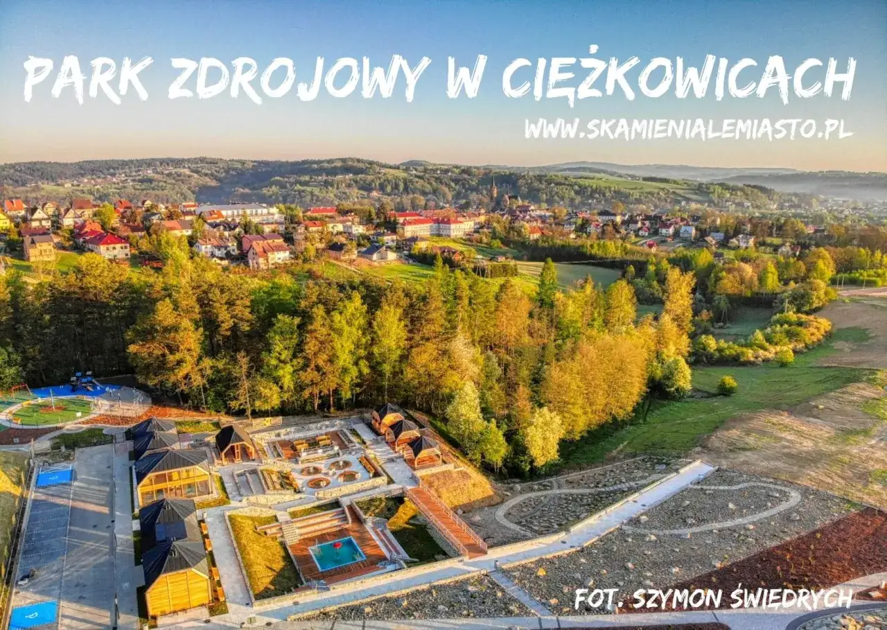 Park zdrojowy w Ciężkowicach, z widokiem na miasto i malownicze wzgórza. Widać nowoczesne obiekty wypoczynkowe, basen i plac zabaw.