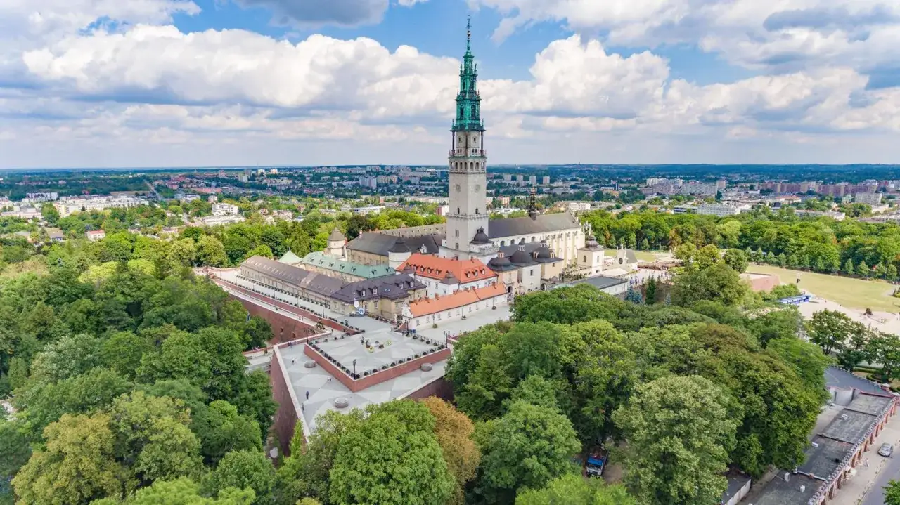 Jasna wieża klasztoru na Jasnej G&oacute;rze g&oacute;ruje nad zielonymi drzewami i zabudowaniami, pokazując co na mieście Częstochowa.