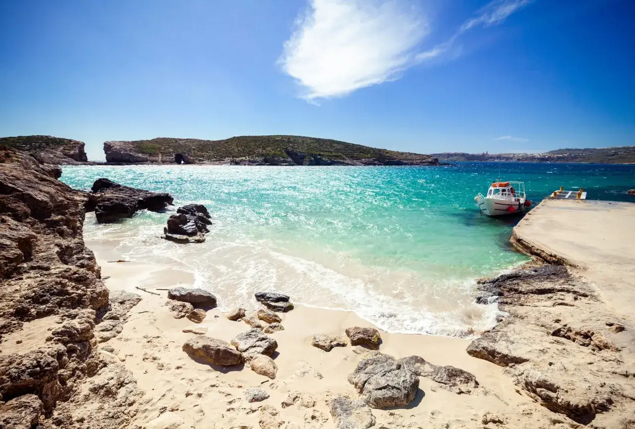 Malta: piaszczyste plaże z turkusową wodą, skałami i łodzią przycumowaną do betonowego molo. Idealne miejsce na relaks.