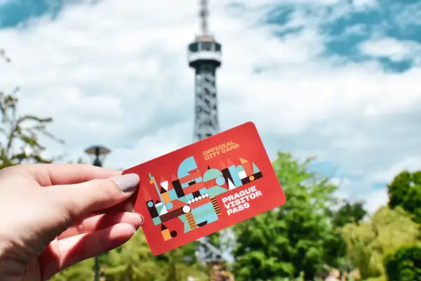 Dłoń trzyma czerwoną kartę "Prague Visitor Pass" na tle wieży widokowej i zielonych drzew.
