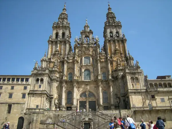 Majestatyczna katedra w Santiago de Compostela z trzema wieżami i schodami, po których wchodzą pielgrzymi.