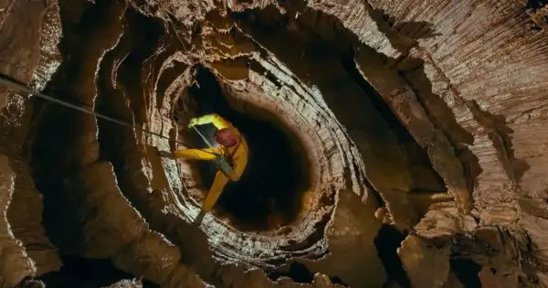 Speleolog w żółtym kombinezonie zjazduje w głąb skalnej otchłani, eksplorując potencjalnie najgłębszą jaskinię na świecie.
