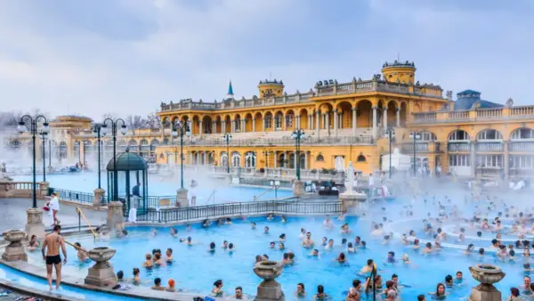 Ludzie kąpią się w gorących źródłach, które są jednymi z najlepszych term w Europie, z piękną, żółtą architekturą w tle.