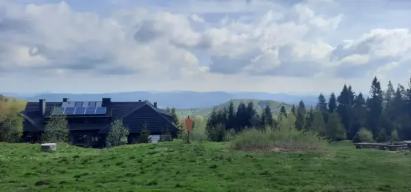 Dom z panelami słonecznymi na tle gór i lasów. Widok na szlaki Jaworzyny Krynickiej.