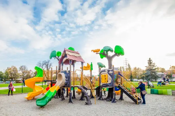 Kolorowy plac zabaw w Krakowie z wieloma zjeżdżalniami i elementami do wspinaczki. Dzieci bawią się wesoło pod błękitnym niebem.