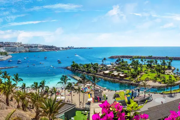 Gran Canaria ciekawostki: malownicza zatoka z plażą, palmami, łodziami i kurortem. Idealne miejsce na wakacje.