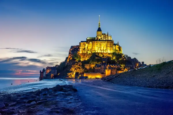 Mont Saint-Michel, jeden z najpiękniejszych zamków w Europie, lśni w blasku wieczornych świateł na tle błękitnego nieba.