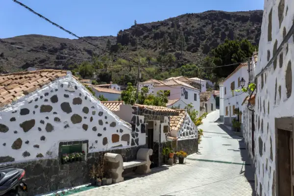 Urocza uliczka z białymi domami i kamiennymi detalami, idealna na gran canaria plan zwiedzania. W tle góry.