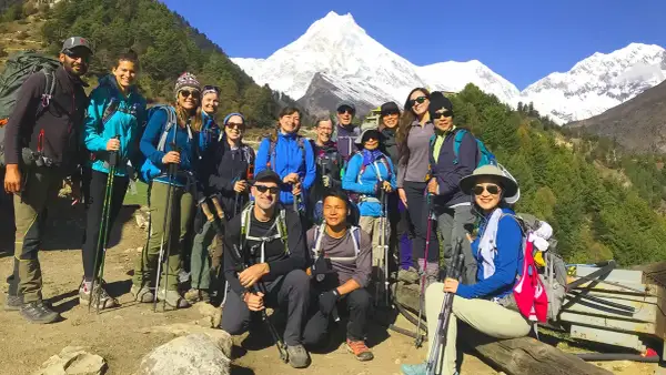 Grupa turystów z plecakami i kijkami trekkingowymi pozuje na tle ośnieżonych gór podczas Manaslu Circuit Trek.