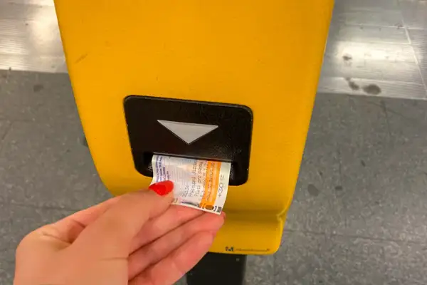 Ręka z czerwoną hybrydą wkłada bilet do żółtego automatu. Praga komunikacja miejska to wygoda podróżowania.
