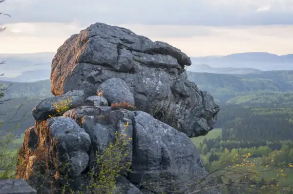 Skalny labirynt na trasie w Górach Stołowych. Majestatyczne formacje skalne na tle zielonych wzgórz i nieba.