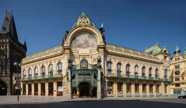 Reprezentacyjny miejski dom w Pradze, z bogatą mozaiką i kopułą, sąsiaduje z gotycką wieżą.