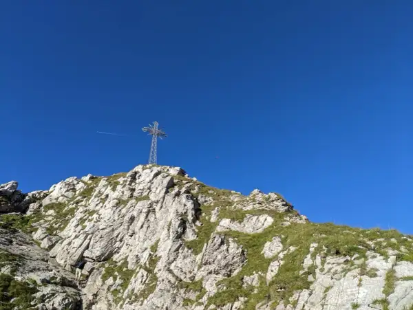 Giewont, śpiący rycerz, wznosi się ku błękitnemu niebu. Na szczycie stoi krzyż, a pod nim skaliste zbocza porośnięte trawą.