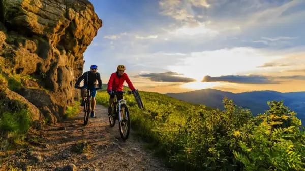 Dwóch rowerzystów przemierza malownicze trasy rowerowe w Polsce, podziwiając zachód słońca nad wzgórzami.