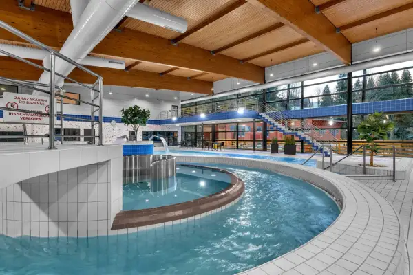 Wodny świat w aquaparku Špindlerův Mlýn: basen z wodospadem, jacuzzi i widokiem na las.