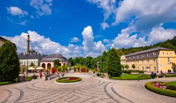 Słoneczny dzień w Kudowie Zdroju. Spacer po urokliwym parku, gdzie piękne budynki i zadbane rabaty kwiatowe tworzą niezapomniane **kudowa zdrój atrakcje**.