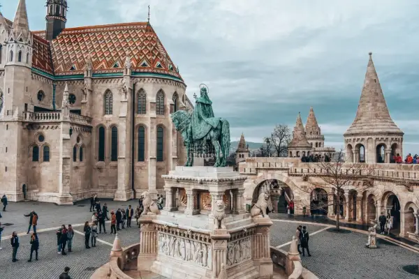 Budapeszt stare miasto: Rycerz na koniu przed kościołem z kolorowym dachem i basztami. Turyści spacerują po brukowanym placu.
